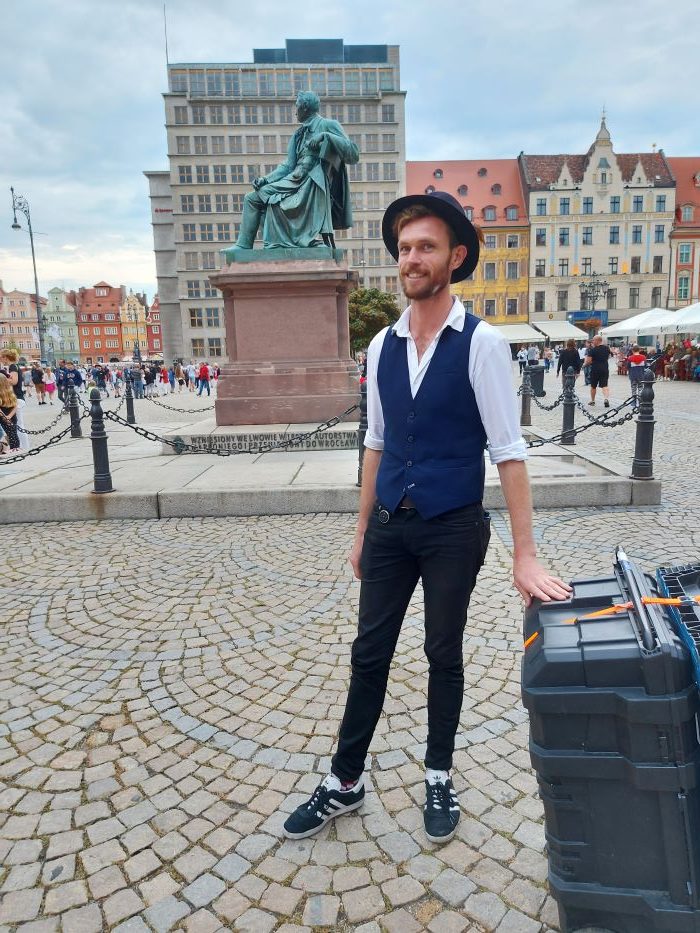 Performer Richard Filby standing in front of Fredro statue in Wroclaw