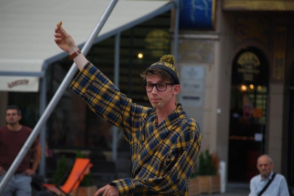 Busker Sam Goodburn podczas pokazu ulicznego prezentuje ciastko, które używa jak rekwizyt cyrkowy.
