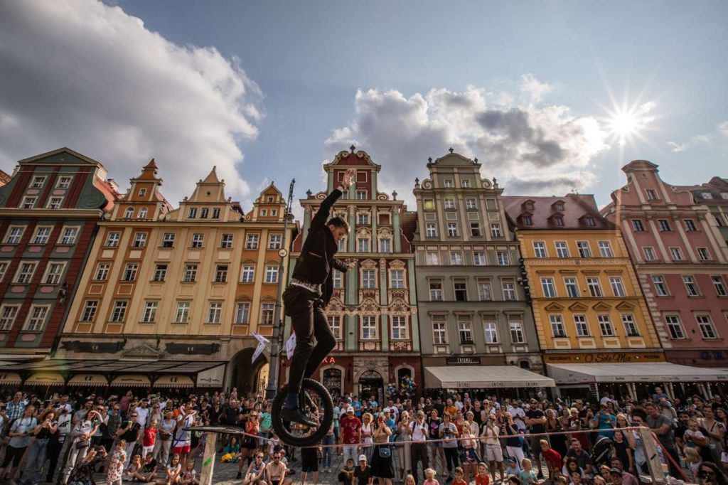 Street performer Sam Goodburn unicycling across the tightrope at BuskerBus 2021 in Wrocław In the back there is a crowd watching him.