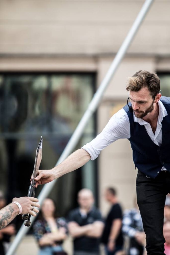 Richard Filby passing juggling props to a volunteer during a street show