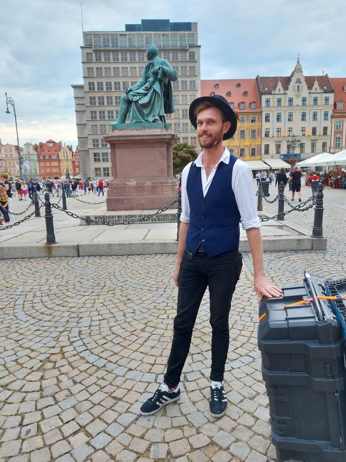 Richard Filby stoi z walizką przed pomnikiem Fredry we Wrocławiu