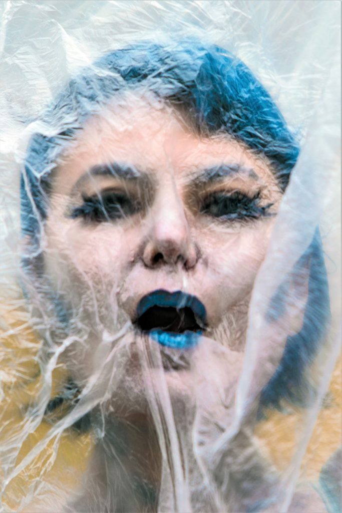 Aktorka Frosso Zagoraiou ma niebieski makijaż i włosy. Do jej twarzy przyklejona jest folla.