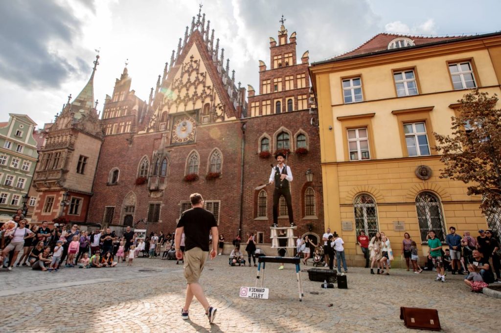 Artysta uliczny Richard Filby balansuje na równoważni i żongluje. W tle wrocławski Ratusz.