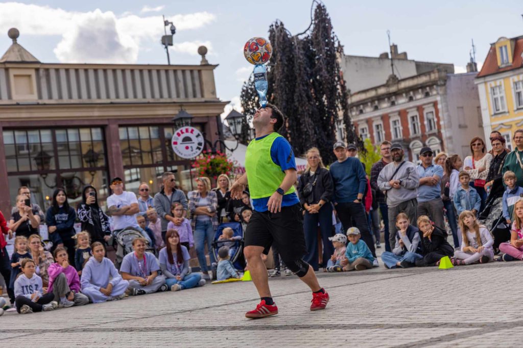 A crowd watches Stefan Florescu performing a trick with a bottle and a football in the city square of Krotoszyn during the street festival Busker Tour.